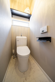 買い置きのペーパーなどを収納できる棚も設置された清潔感あふれるトイレ。・トイレＴＯＴＯウォシュレット一体型便器「ＺＪ1」：ホワイト・フロアシートサンゲツ「ＨＭ-10108」・壁クロスサンゲツ「ＳＰ-9562」