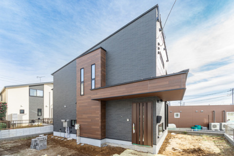 木肌調のサイディングがアクセントになっているモダンな外観デザイン。・外壁材ベース：旭トステムAT-WALL15P　スヴェルトP（スヴェルトチャコールP）・外壁材アクセント：旭トステムAT-WALL15P　ラスティウッドP（ラスティブラウンP）・玄関ドア：YKKAPヴィナートD30（ショコラウォールナット）