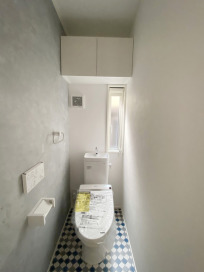 予備のトイレットペーパーやタオル、カバーなどを収納できる物入れも設置されたトイレ空間。床の柄がモダンな空間を演出しています。
