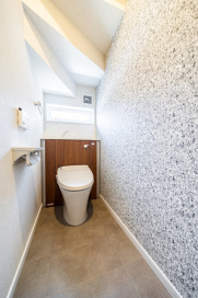 階段下のスペースを上手に利用したトイレ。アクセントクロスの柄は、実はウォーリーに！・LIXILベーシアピタ（オフホワイト/クリエモカ）・タオルリング：LIXIL（KF-AA70P）・アクセントクロス：シンコール（BA5546）